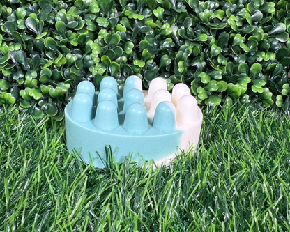 Scrub shaped bar of mint and eucalyptus soap that is a mix of a medium-dark green and white, displayed on a grass like surface.