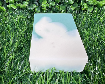 Rectangular shaped bar of mint and eucalyptus soap that is a mix of a medium-dark green and white, displayed on a grass like surface.
