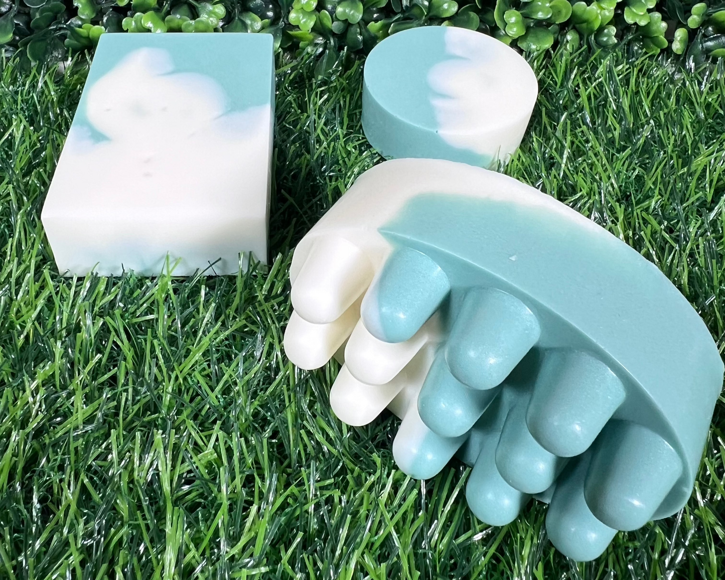 A variety of homemade bar soaps with mint and eucalyptus, displayed on a grass-like surface.