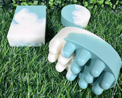 A variety of homemade bar soaps with mint and eucalyptus, displayed on a grass-like surface.