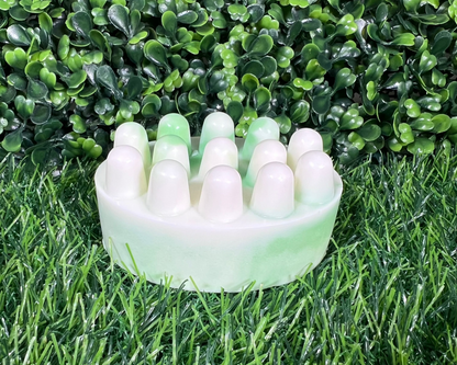 Scrub shaped sage soap that is a mix of a light green and white, displayed on a green surface.