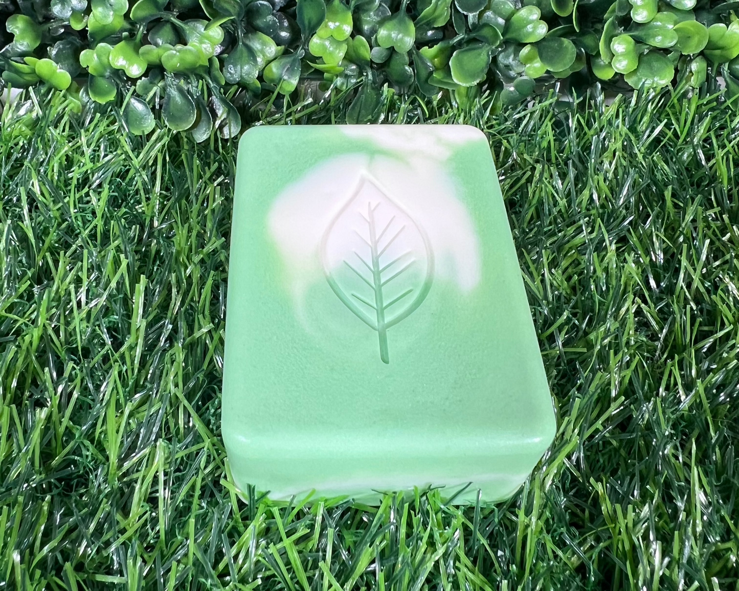 Rectangular sage soap with rounded edges and leaf design on top that is a mix of a light green and white, displayed on a green surface.