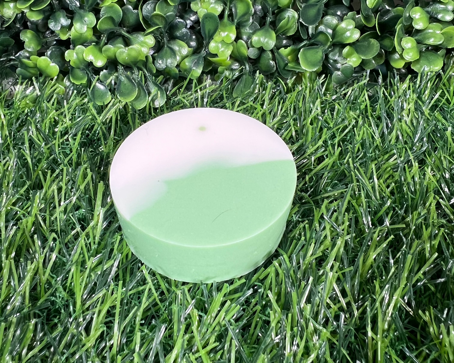 Circular sage soap that is a mix of a light green and white, displayed on a green surface.