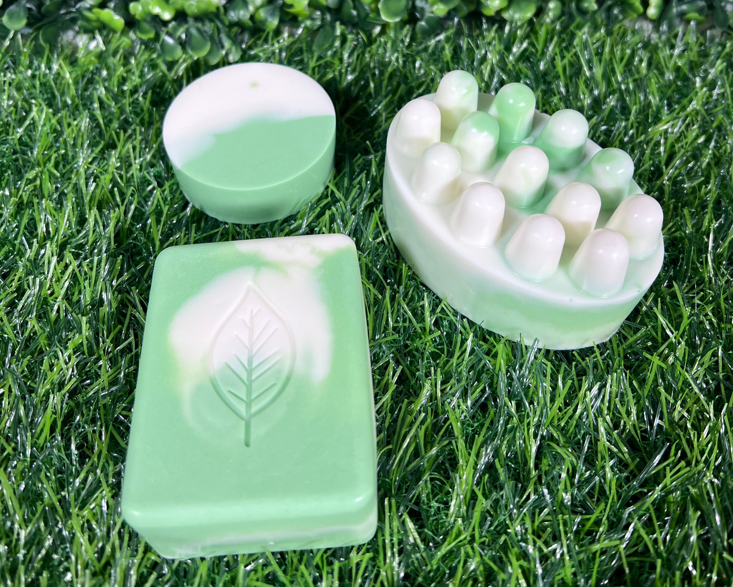A variety of homemade sage bar soaps in different shapes and sizes, displayed on a green leaf like surface.