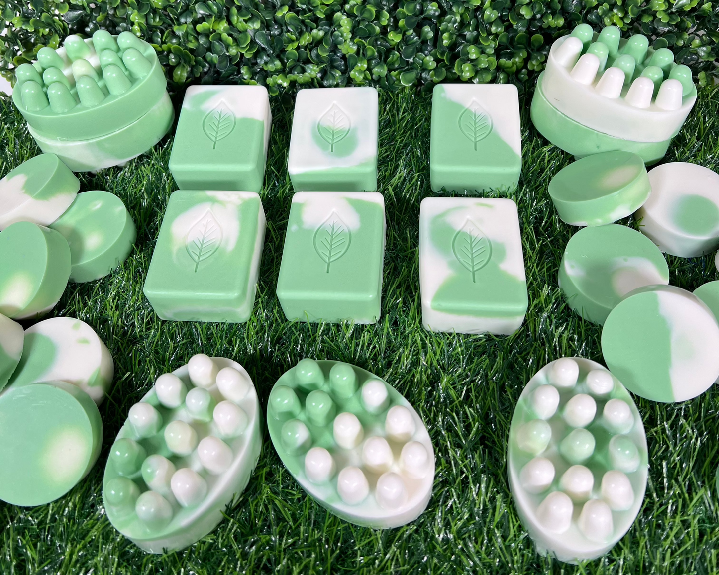 A variety of homemade sage bar soaps in different shapes and sizes, displayed on a green leaf like surface.