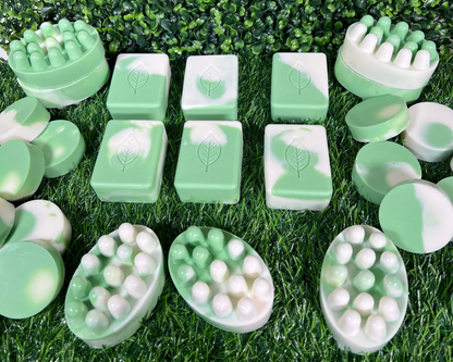 A variety of homemade sage bar soaps in different shapes and sizes, displayed on a green leaf like surface.