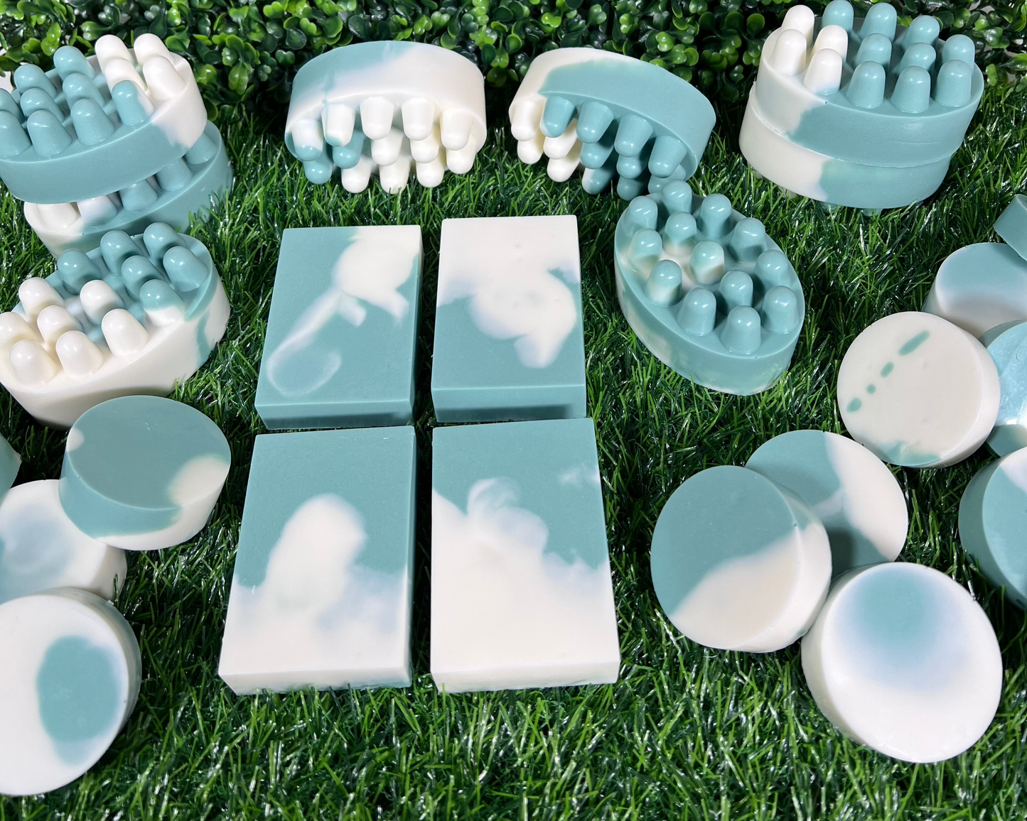 A variety of homemade bar soaps with mint and eucalyptus, displayed on a grass-like surface.
