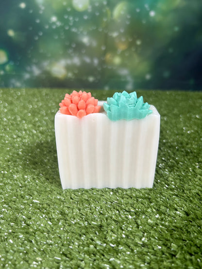 Rectangular wavy soap with an orange and green succulent decorations on top of the white bar that is on a green grass-like surface