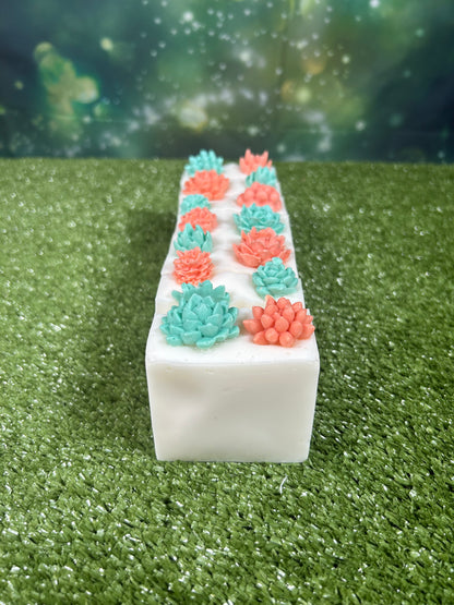 Long white rectangular soap block with decorative alternating green and orange succulent-like designs on a green textured surface