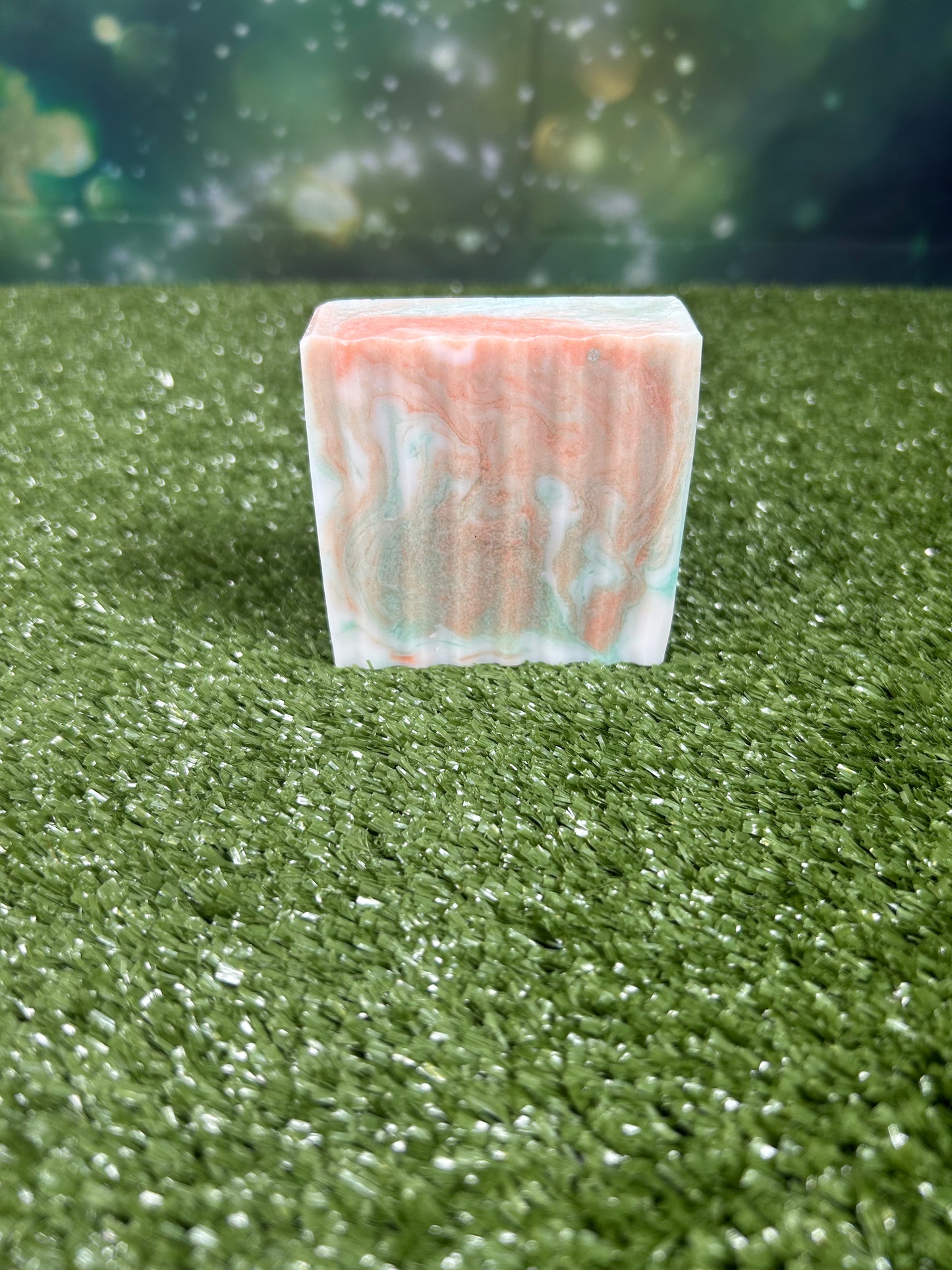 Rectangular bar of soap with orange and green marbled pattern on a green grass-like surface