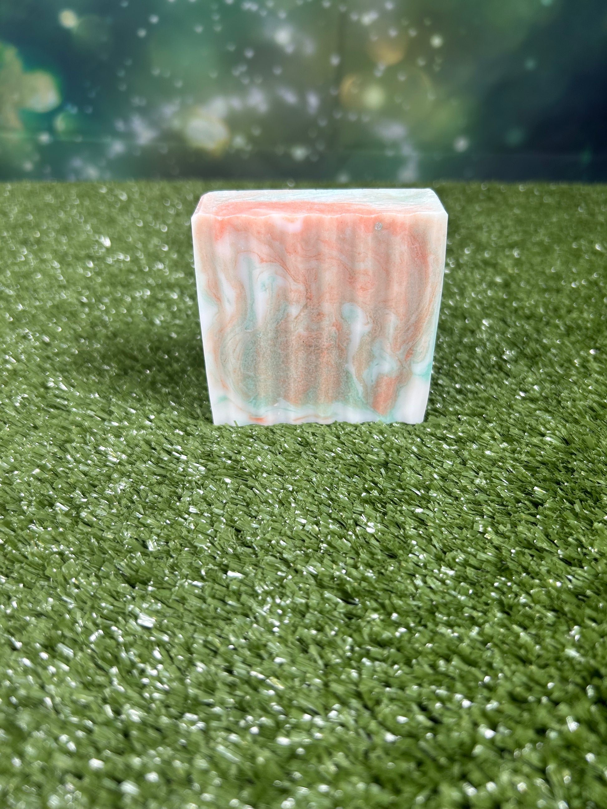 Rectangular bar of soap with orange and green marbled pattern on a green grass-like surface