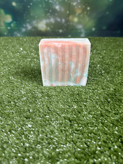Rectangular bar of soap with orange and green marbled pattern on a green grass-like surface