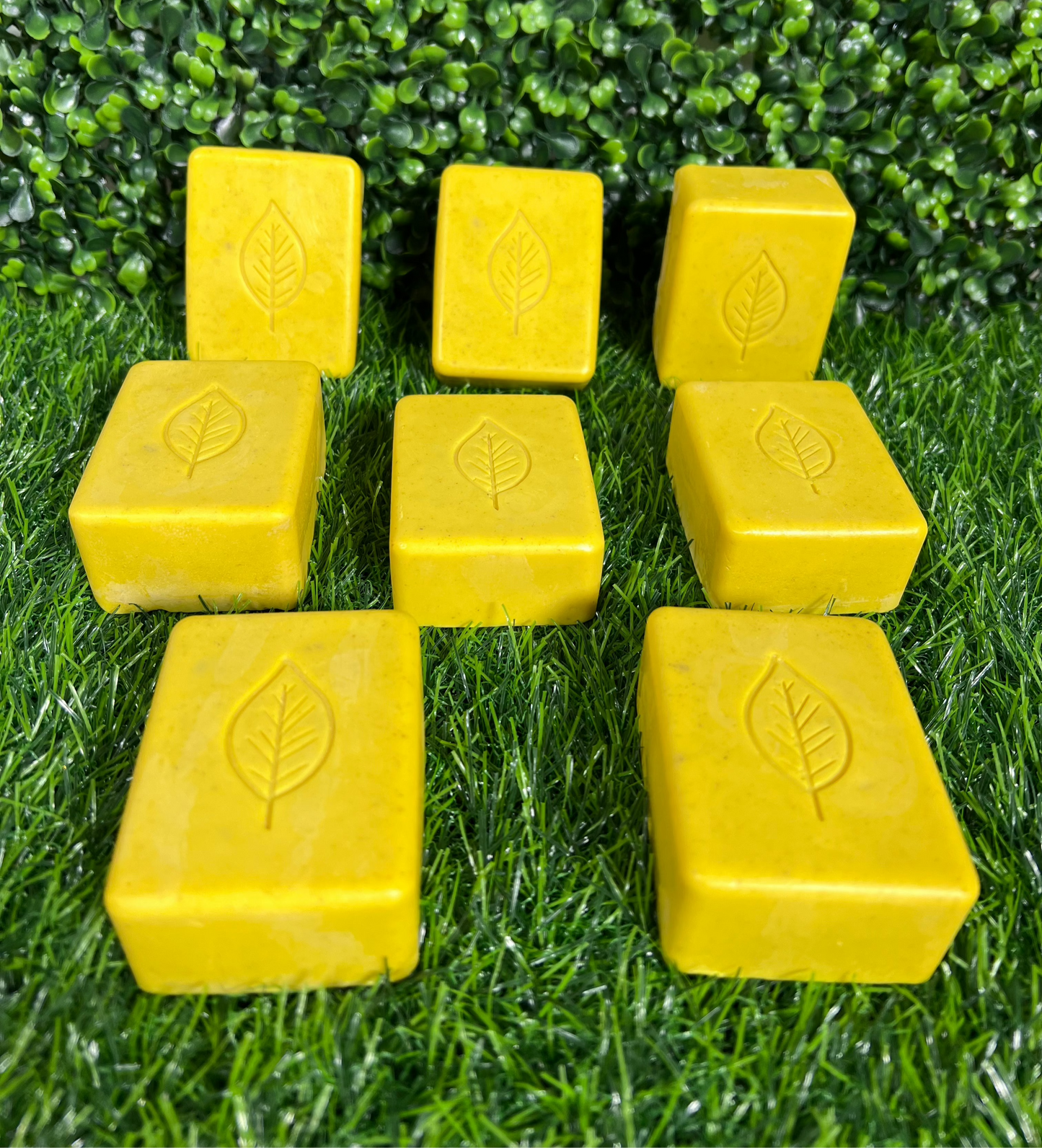 A collection of yellow turmeric bar soaps with leaf imprints, arranged on a grass-like surface.