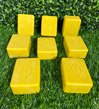 A collection of yellow turmeric bar soaps with leaf imprints, arranged on a grass-like surface.