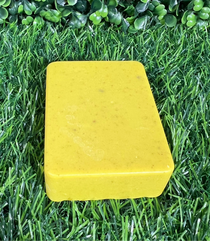 Rectangular turmeric yellow bar of soap with rounded edges, displayed on a green grass-like surface.