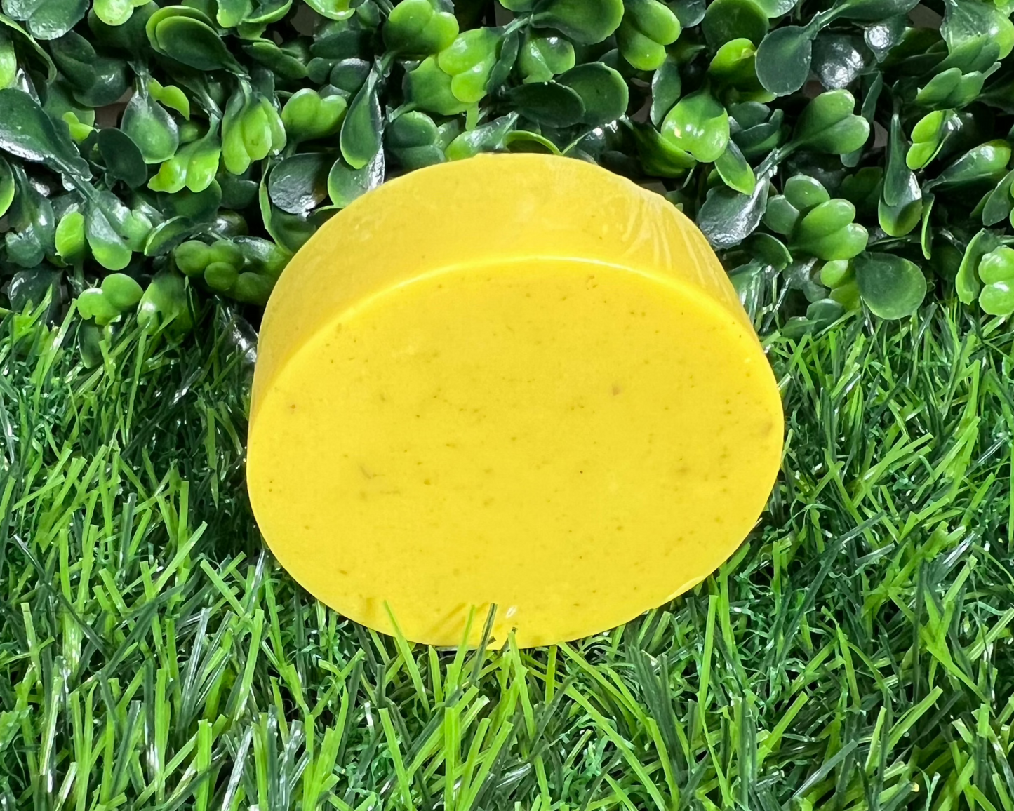 Circular bar of soap that is turmeric yellow and displayed on a leaf like surface.