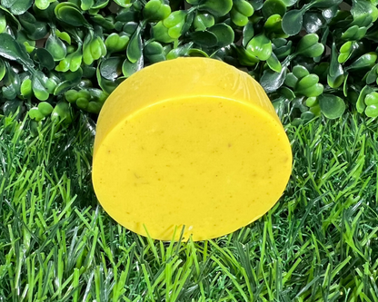 Circular bar of soap that is turmeric yellow and displayed on a leaf like surface.