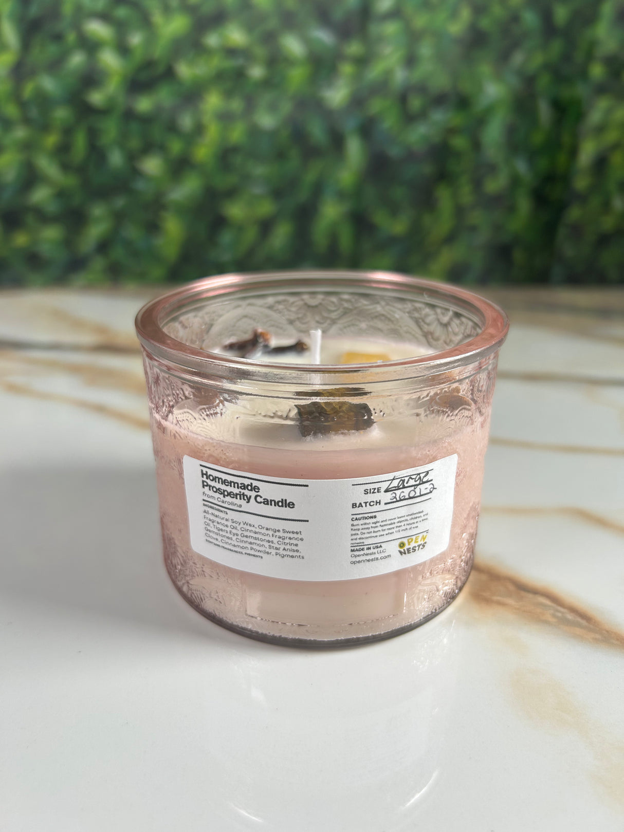 Candle in a large pink glass container with a label 