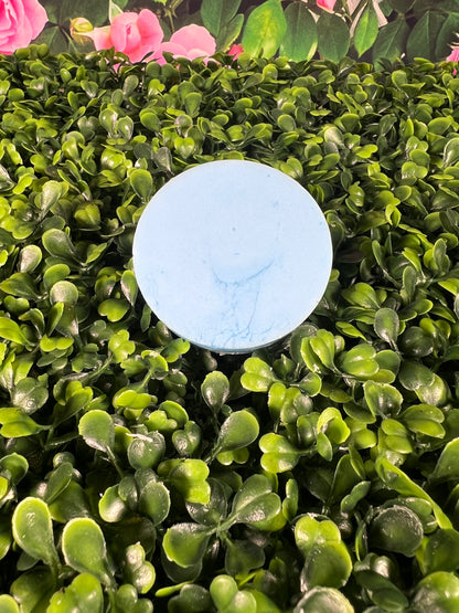 Circular light blue bar of soap displayed on a leaf like surface.