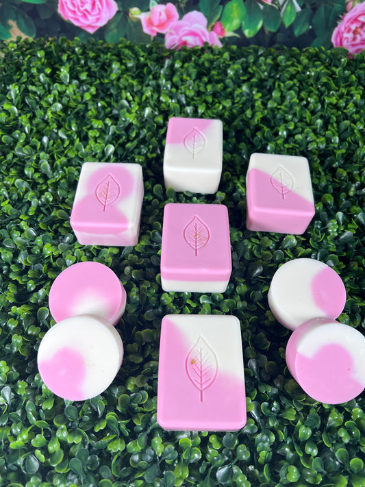 A variety of bar soaps with a pink and white swirl pattern, displayed on a green surface with pink flowers in the background.