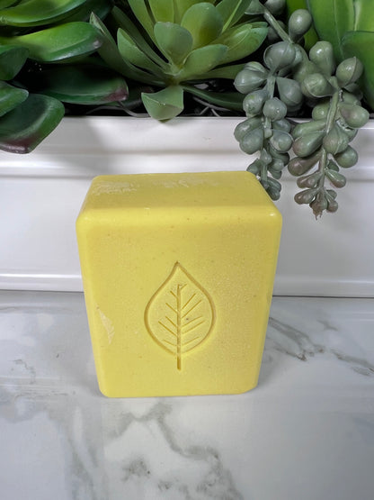 Rectangular bar of yellow turmeric soap with rounded edges and a leaf design on it, displayed on a marble surface.