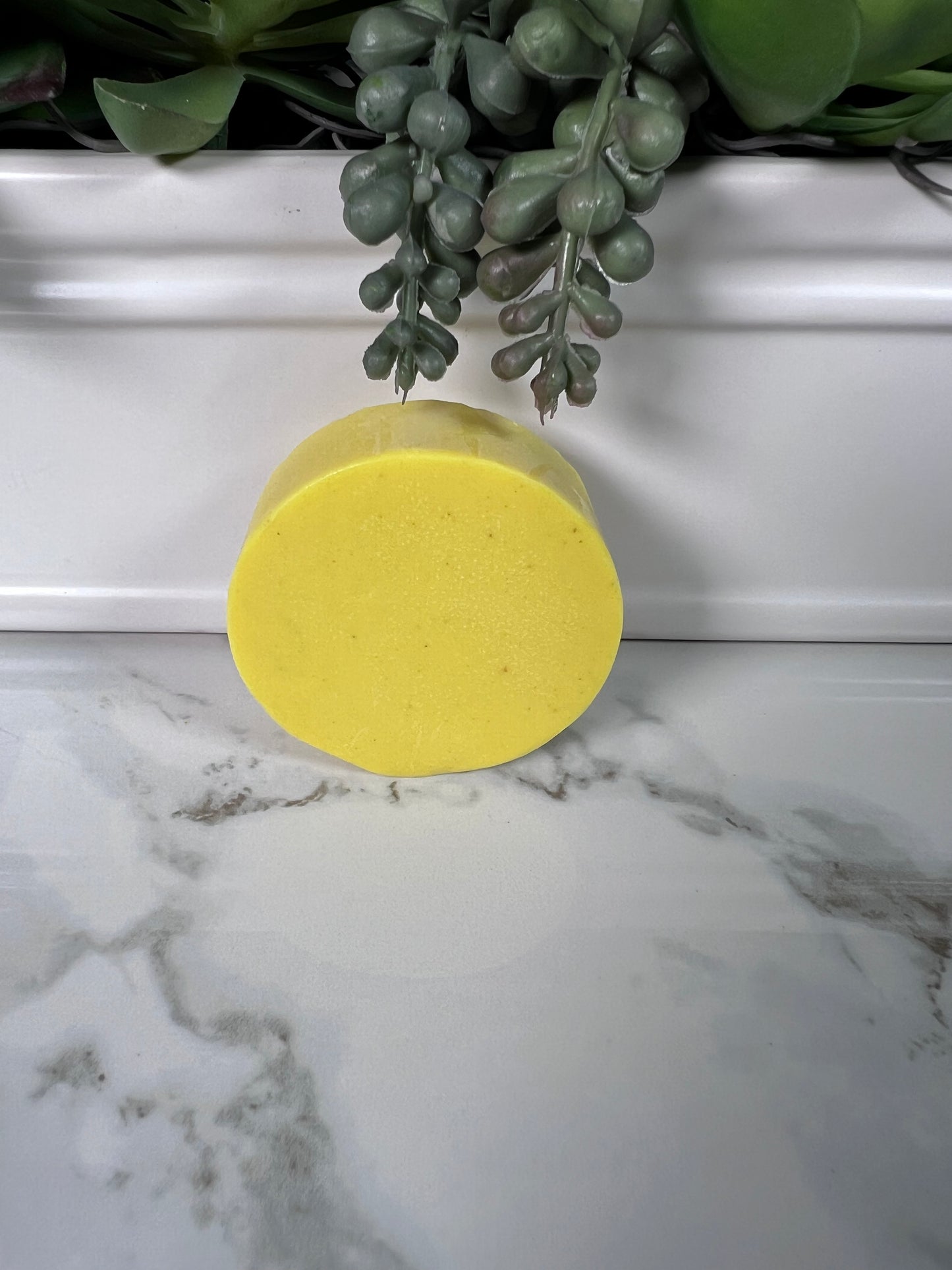 Circular bar of yellow turmeric soap on a marble surface.