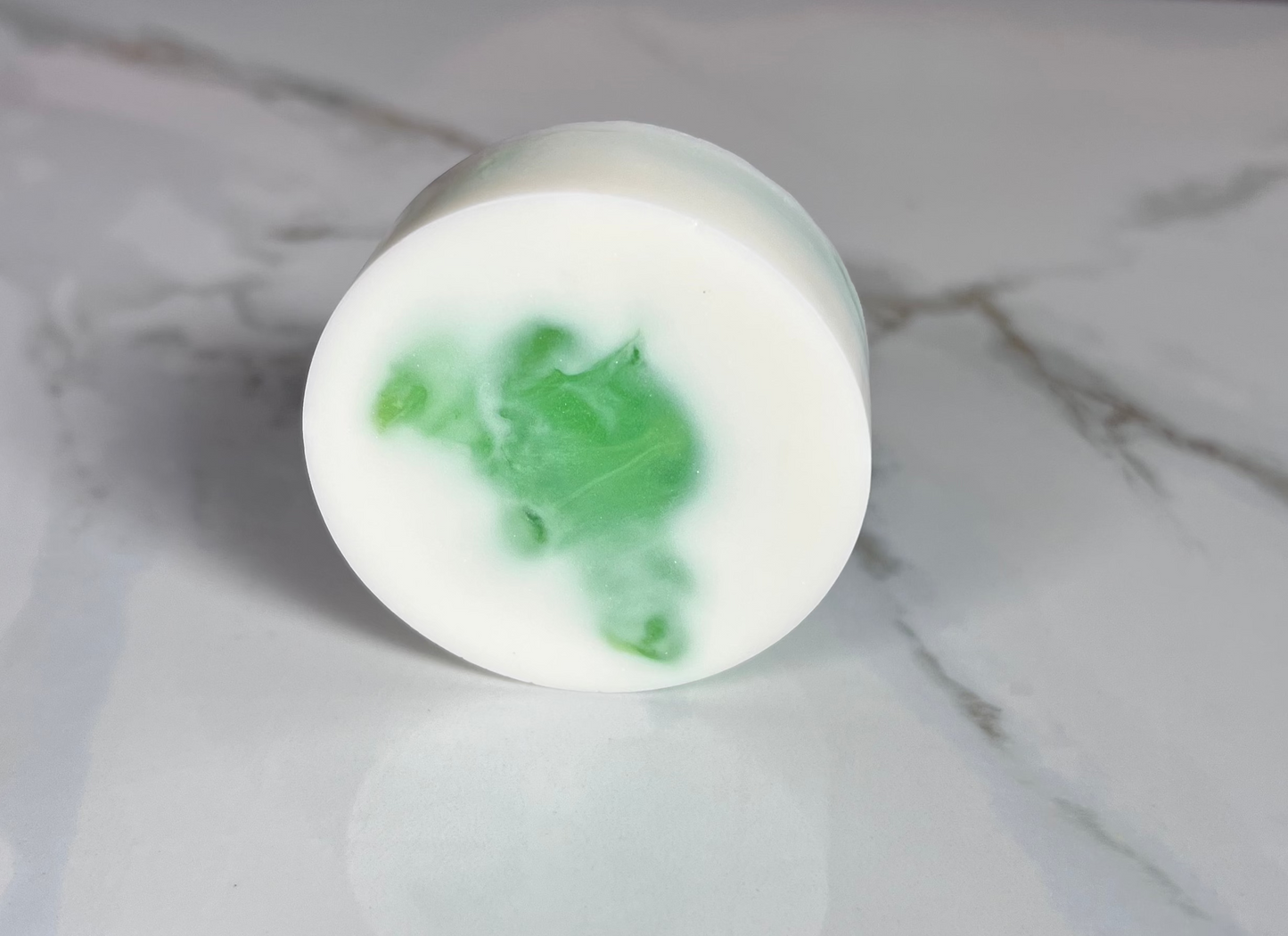Round white soap with a bit of green on a marble surface