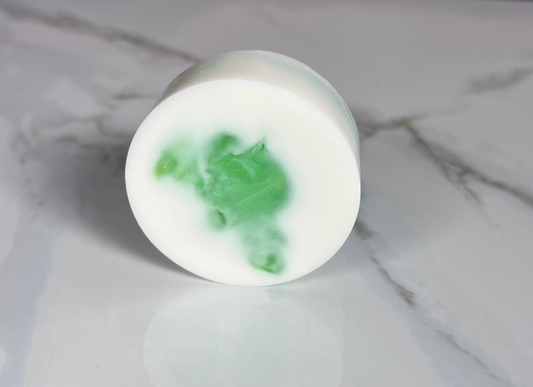 Round white soap with a bit of green on a marble surface