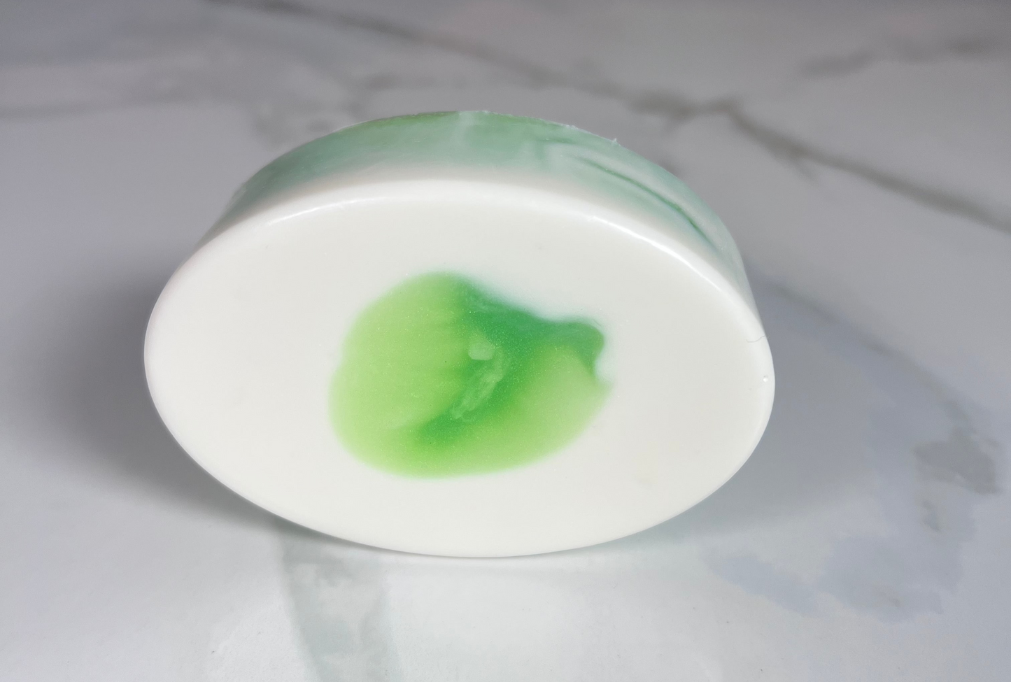 White oval-shaped bar of soap with bits of green throughout on top of a marble background