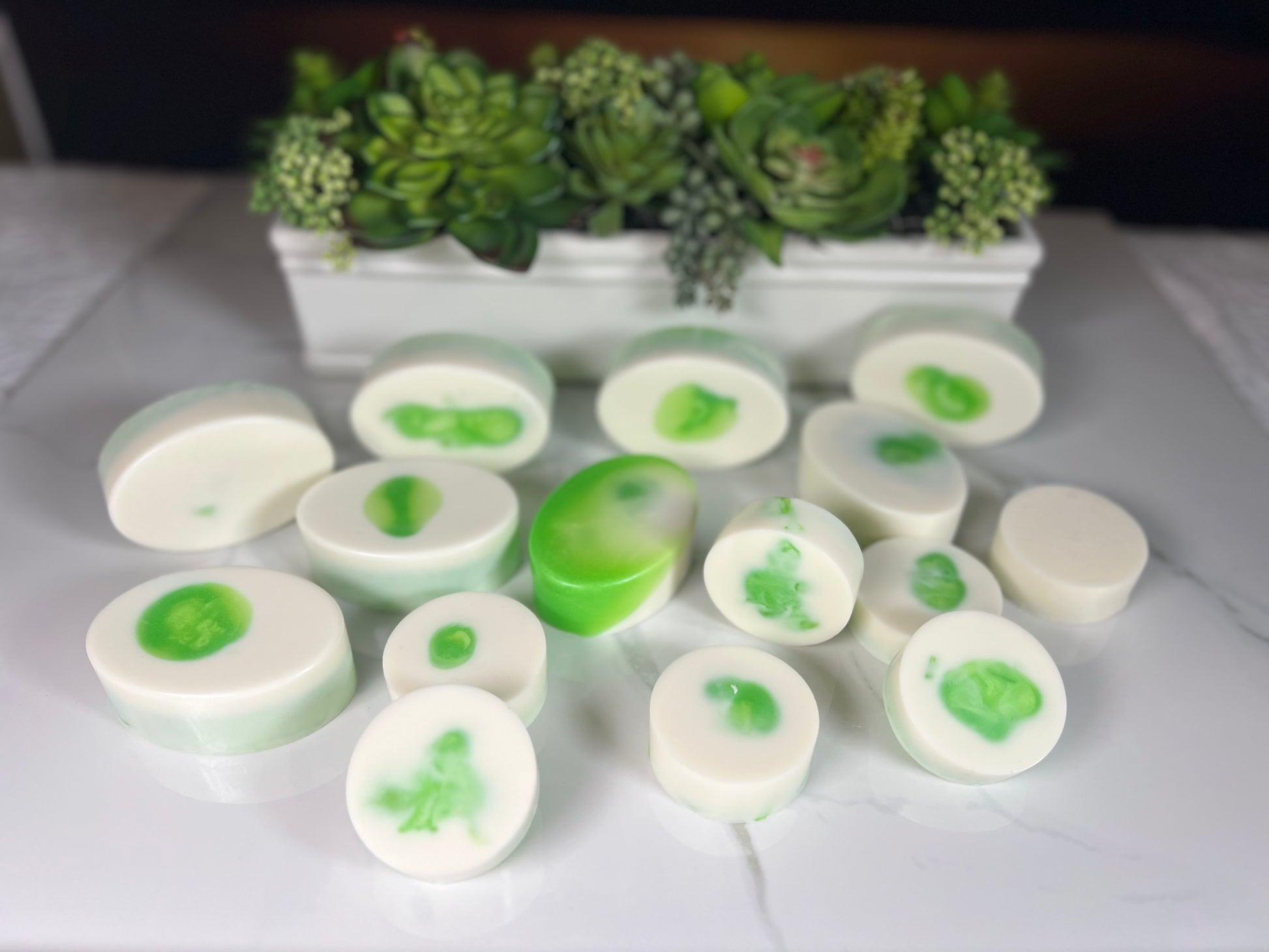 Many green and white soap bars with a plant in the background